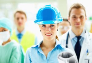 Beautiful cute young female architect in blue helmet smiling with people standing behind